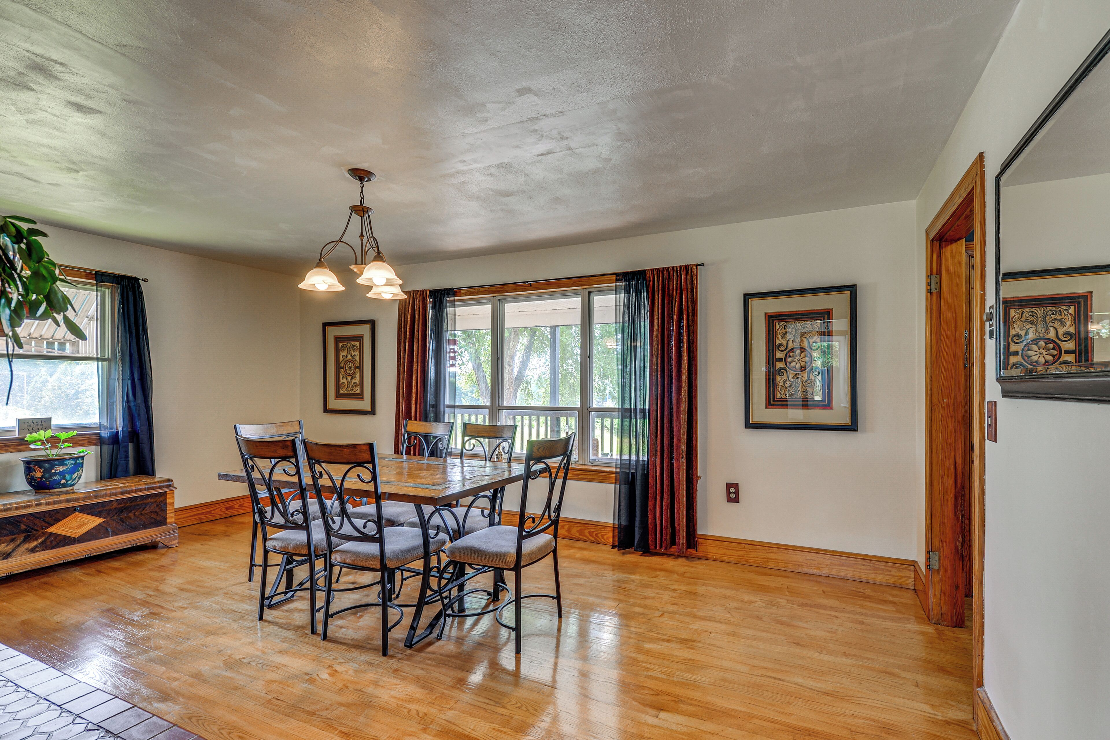 A dining area with a wooden table and chairs, a chandelier, and large windows with curtains.
