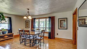 A dining area with a wooden table and chairs, a chandelier, and large windows with curtains.