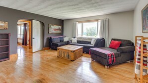 A spacious living room with hardwood flooring, a large window with curtains, and a cozy seating area with a sofa and armchairs. - Quiet Stuart Retreat w/ Yard & Fireplace (Patrick Springs)