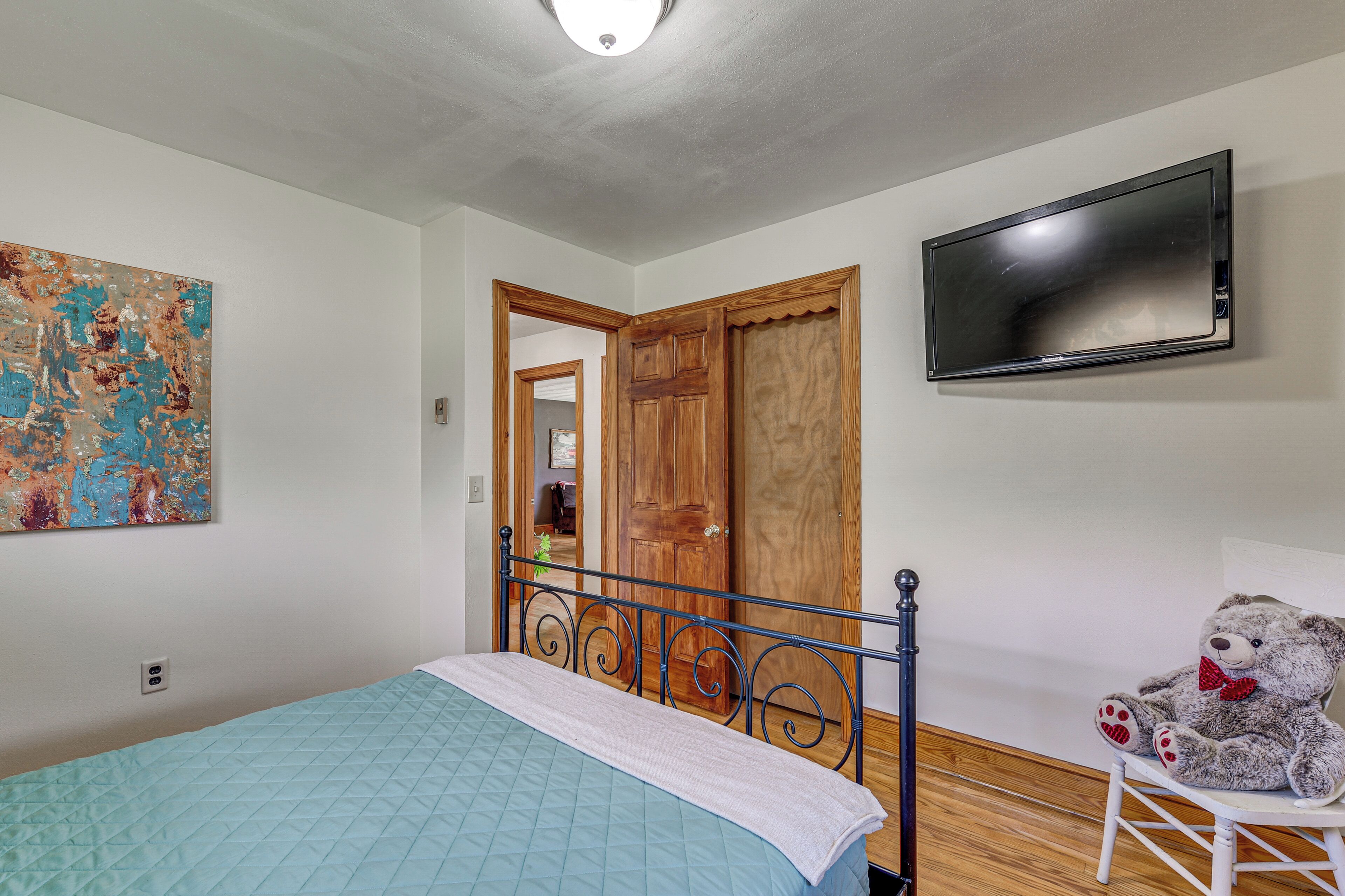 A bedroom with a bed, a television mounted on the wall, and a teddy bear on a chair.