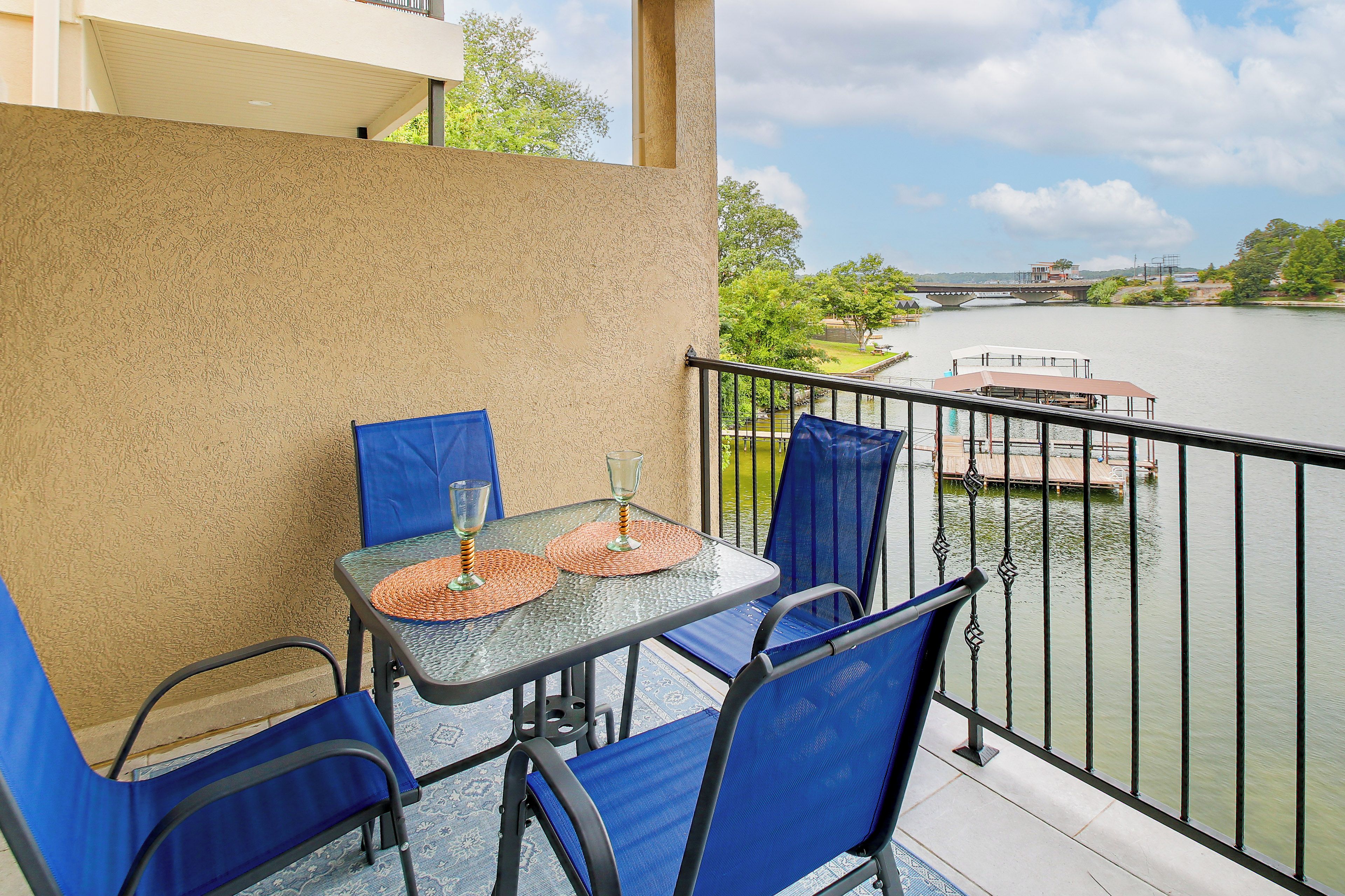 A balcony with a table and chairs, overlooking a river with a bridge and greenery.