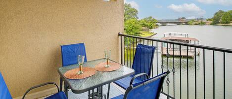 A balcony with a table and chairs, overlooking a river with a bridge and greenery.