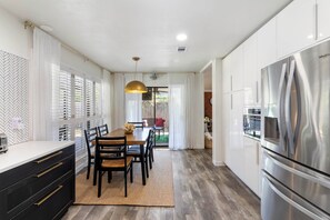 A modern kitchen with a large stainless steel refrigerator, wooden dining table, and black chairs. - The Oaks at Aggieland! Modern Home w/ Patio & Yard (Bryan)