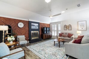 Een woonkamer met een wand van visgraatparket, een open haard, een bank, een salontafel en een televisie.