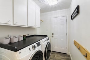 Ein Waschraum mit einer Waschmaschine mit Frontlader, weißen Schränken und einer Tür mit der Aufschrift 'WASHROOM'.