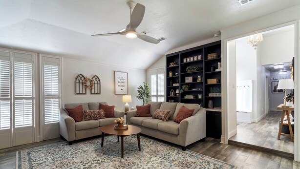 A living room with a ceiling fan, a sofa set, a coffee table, a patterned rug, and a bookshelf. - The Oaks at Aggieland! Modern Home w/ Patio & Yard (Bryan)