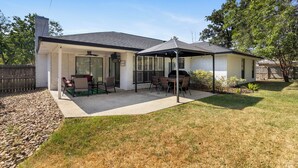 A residential backyard with a covered patio area, a grill, and a seating arrangement. - The Oaks at Aggieland! Modern Home w/ Patio & Yard (Bryan)