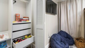 A child's playroom with a white shelving unit, a television, and a cozy seating area with a blue cushion and a basket. - The Oaks at Aggieland! Modern Home w/ Patio & Yard (Bryan)