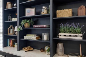 Een donkere boekenkast met diverse decoratieve objecten, waaronder een lijst met de Amerikaanse vlag, een boek getiteld 'Aggieland 2004' en een houten dienblad met lavendelplanten.