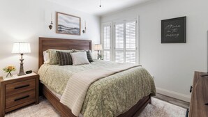 A bedroom with a bed, nightstands, a lamp, a clock, a ceiling fan, a painting, and a wall with a motivational quote. - The Oaks at Aggieland! Modern Home w/ Patio & Yard (Bryan)