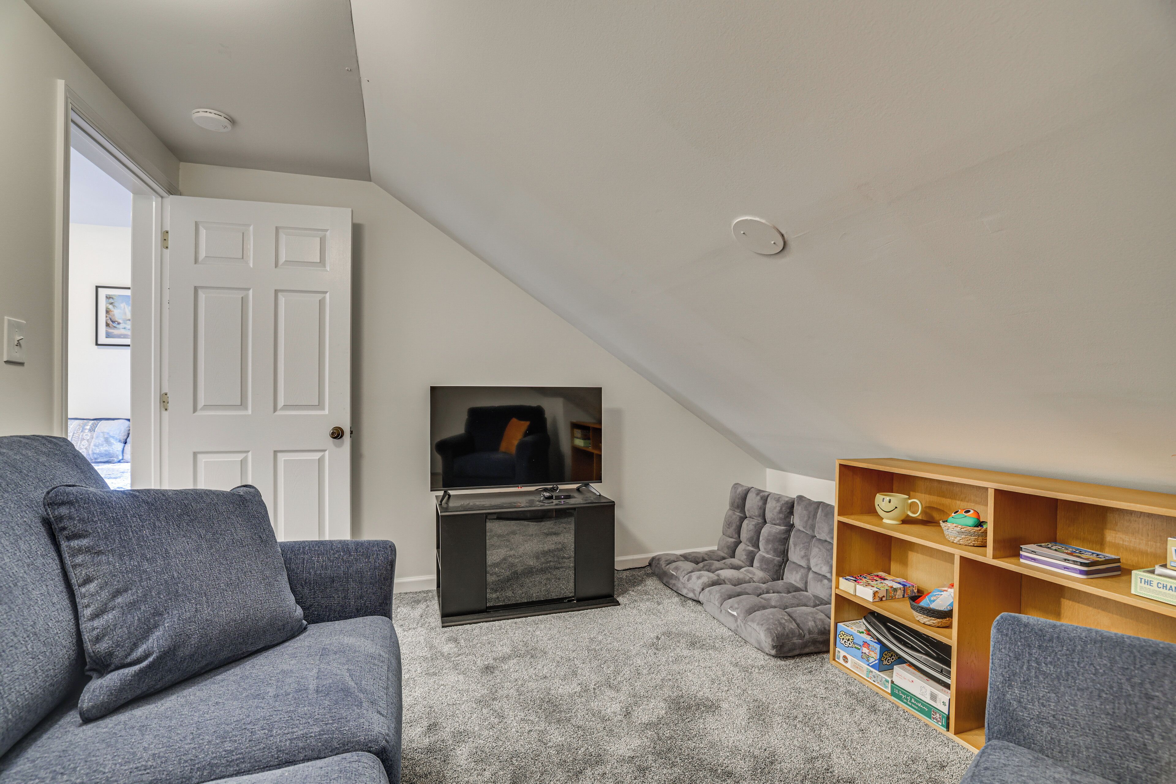 A living room with a grey sofa, a television, a bookshelf, and a door leading to another room.