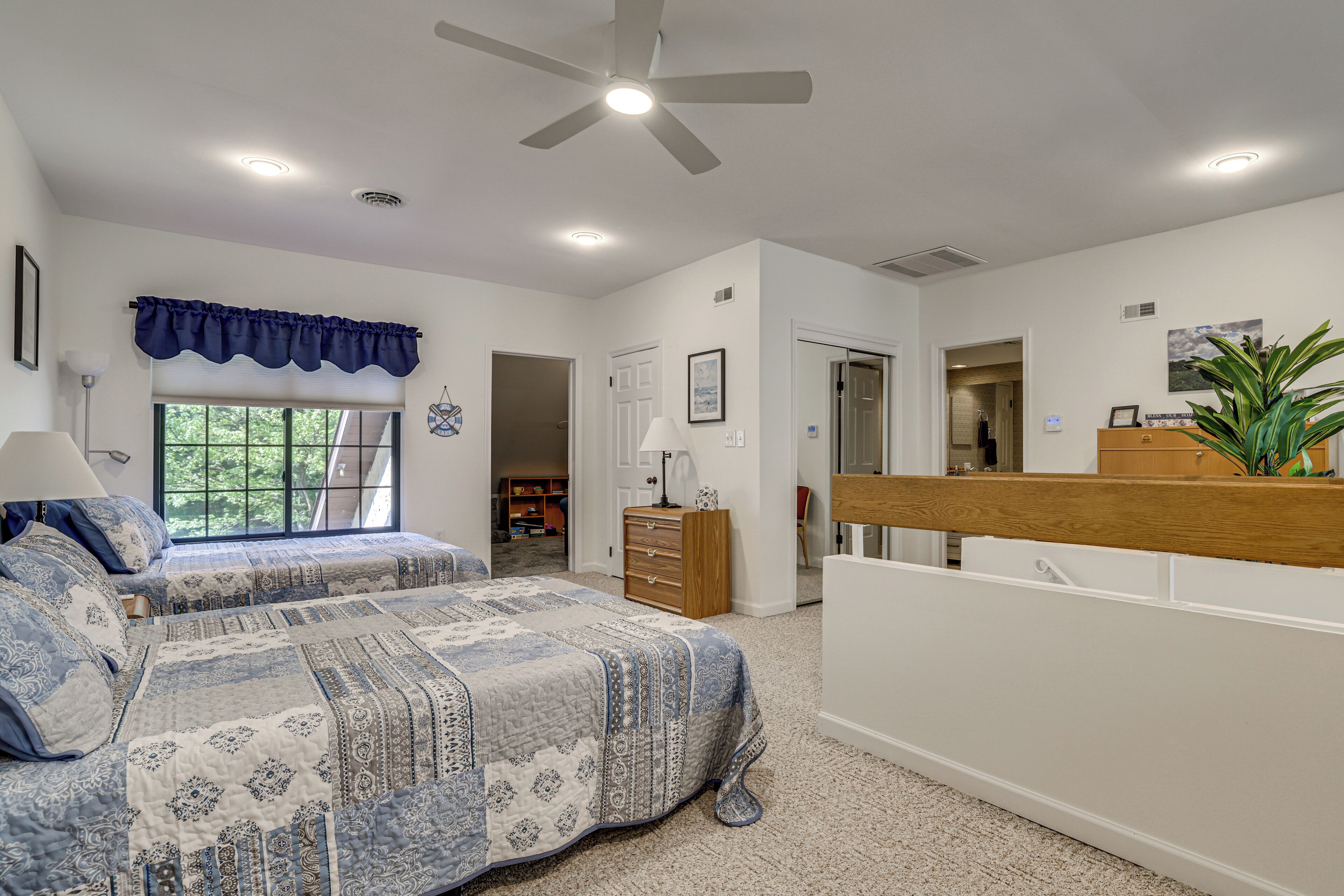 A bedroom with two beds, a ceiling fan, and a window with a view of trees.