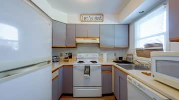 A compact kitchen with a white stove, a microwave, and a sink. There's a sign above the stove that reads 'let's eat'.