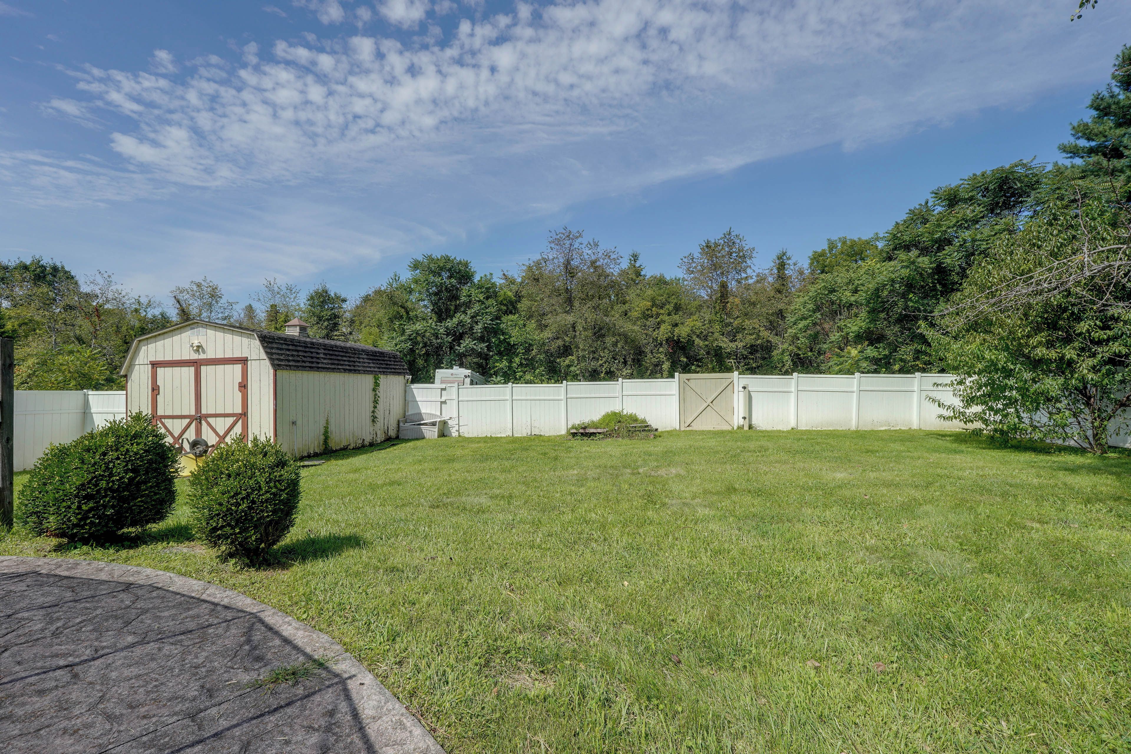 A fenced backyard with a shed, a well-maintained lawn, and dense trees in the background.