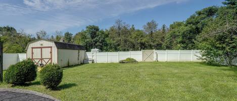 A fenced backyard with a shed, a well-maintained lawn, and dense trees in the background.