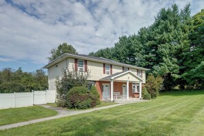 A two-story house with a front porch, a small garden, and a white fence. - Patio + Yard: Extended Escape in Hudson Valley! (Highland)