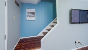 Una scala con gradini in legno che porta a un pianerottolo, un quadro appeso al muro e un televisore Samsung montato sulla parete.