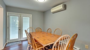 Una sala da pranzo con un tavolo in legno e sei sedie, una porta scorrevole in vetro e un condizionatore d'aria a parete.