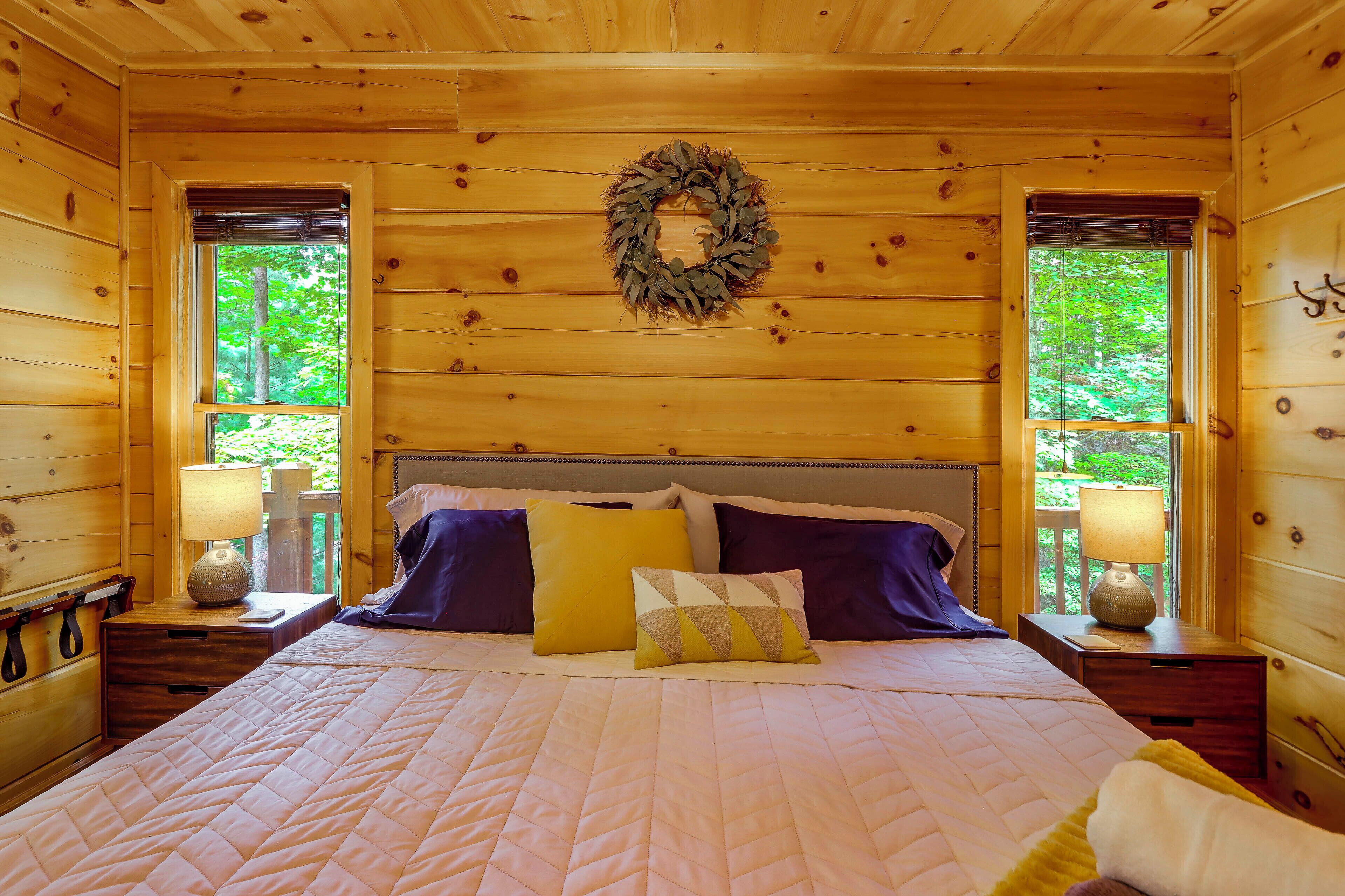 Ein Schlafzimmer einer Holzhütte mit Bett, Kissen, Nachttischen und einem Kranz an der Wand.