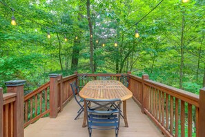 A wooden deck with a table and chairs, surrounded by lush greenery. - Private Hot Tub & Deck! Cherry Log Gem (Blue Ridge)