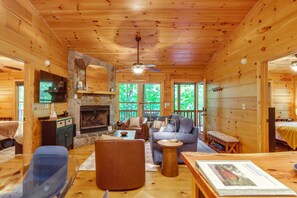 A cozy cabin interior with a stone fireplace, wooden walls, and a ceiling fan. - Private Hot Tub & Deck! Cherry Log Gem (Blue Ridge)