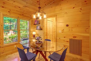 A wooden interior with a round glass table, four chairs, a chandelier, and a view of greenery outside. - Private Hot Tub & Deck! Cherry Log Gem (Blue Ridge)