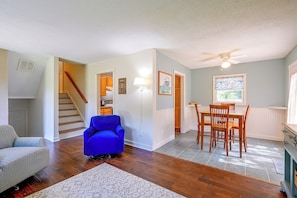 A spacious living area with hardwood flooring, a blue armchair, a dining table with chairs, and a staircase leading to another level. - Centrally Located Adventure Basecamp in King! (King)