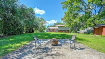 A backyard with a fire pit, two chairs, and a house in the background.