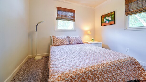 Een slaapkamer met een bed, nachtkastje, lamp en een raam met zonwering.