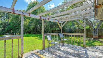 A wooden deck with a pergola structure, outdoor seating, and a grassy yard.