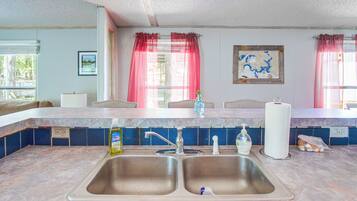A kitchen with a double sink, a window with curtains, a map on the wall, and a bottle of dish soap on the counter.