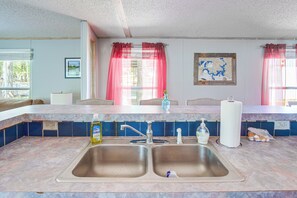 A kitchen with a double sink, a window with curtains, a map on the wall, and a bottle of dish soap on the counter.