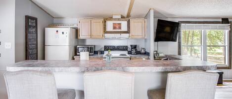 A kitchen with a central island, bar stools, a refrigerator, a microwave, a stove, and a television.