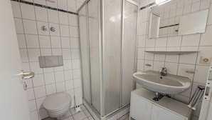 A bathroom with a toilet, a shower enclosure, a sink, and a mirror.