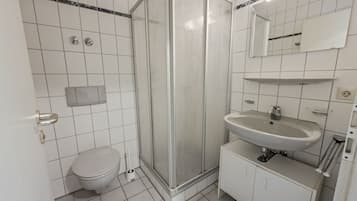 A bathroom with a toilet, a shower enclosure, a sink, and a mirror.
