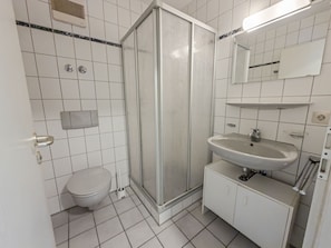 A bathroom with a toilet, a shower enclosure, a sink, and a mirror. - Nagold Quartier (Nagold)
