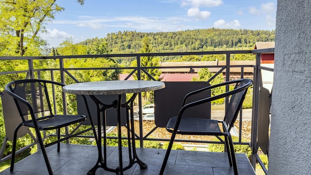 A balcony with two chairs and a table, overlooking a forested hillside.