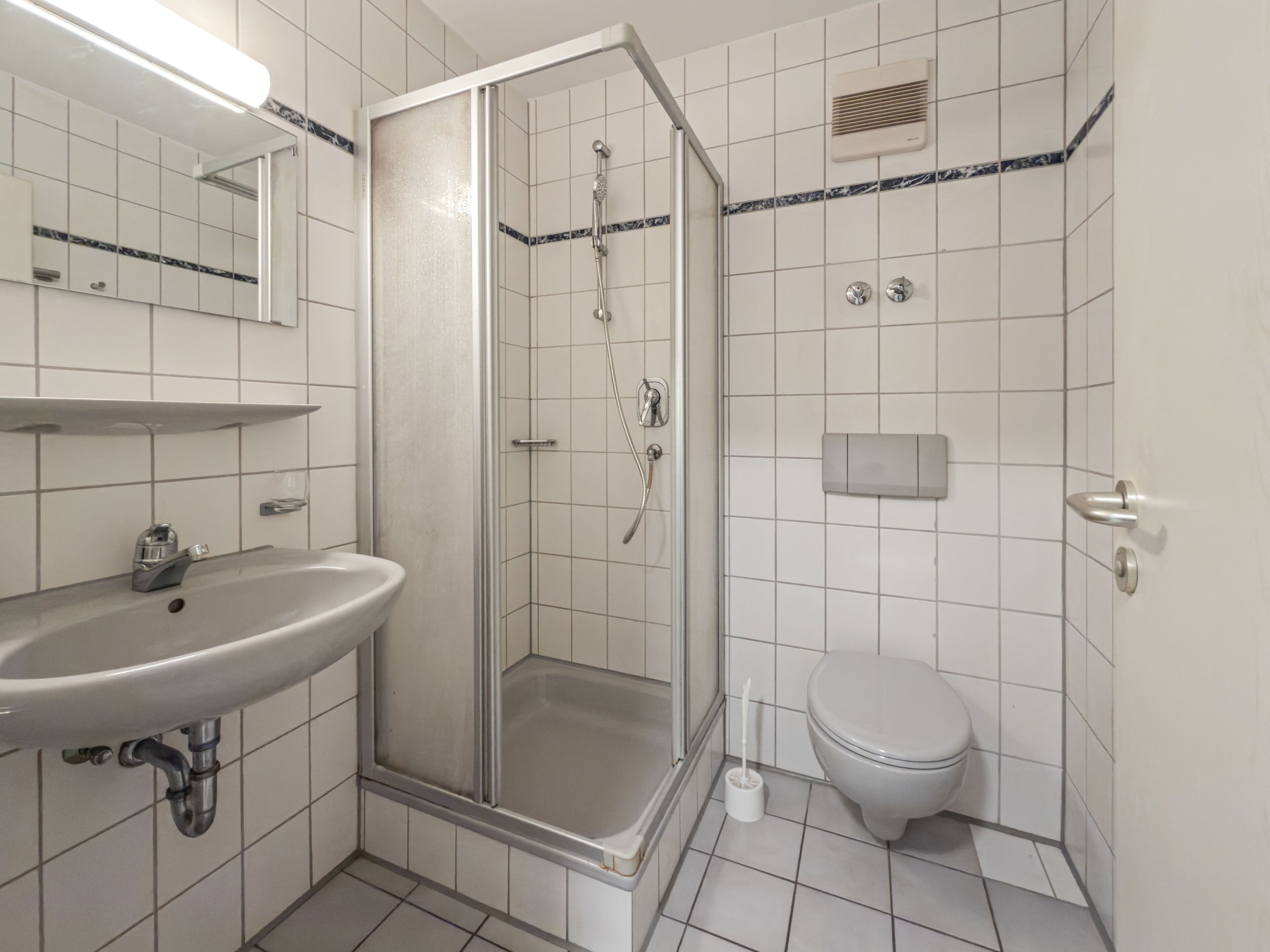 A bathroom with a shower, toilet, sink, and a mirror.
