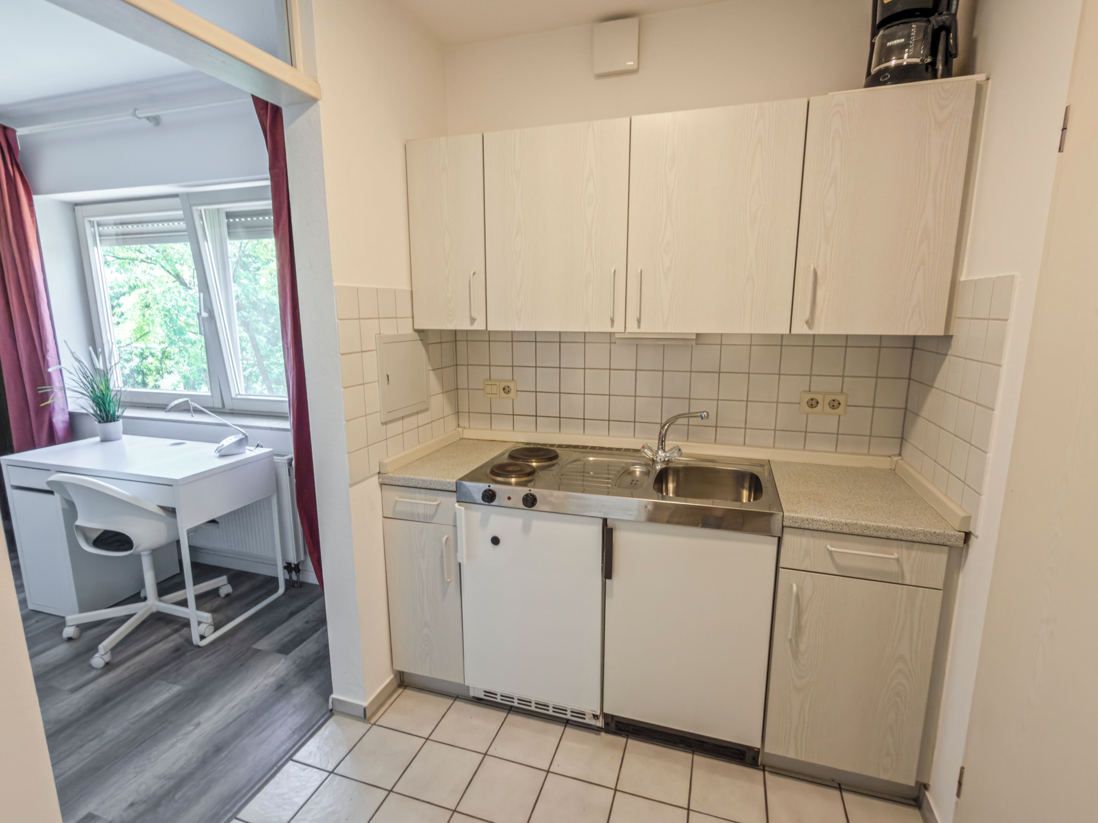 A compact kitchen with white cabinetry, a built-in dishwasher, and a stove.
