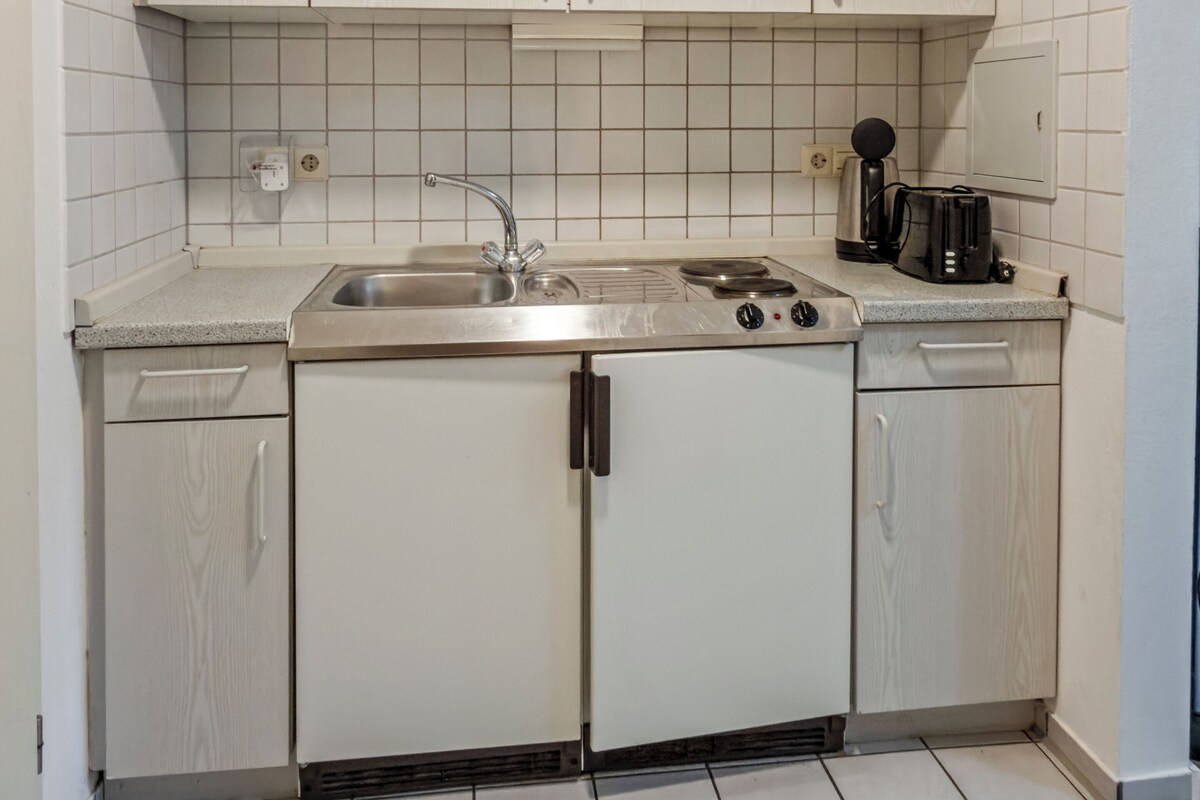 A compact kitchen with white cabinets, a stainless steel sink, and a coffee maker.