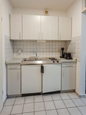 A compact kitchen with white cabinets, a stainless steel sink, and a coffee maker.