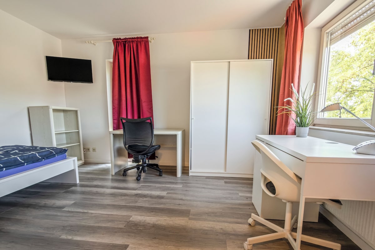 A bedroom with a bed, a desk, a chair, a wardrobe, and a television.