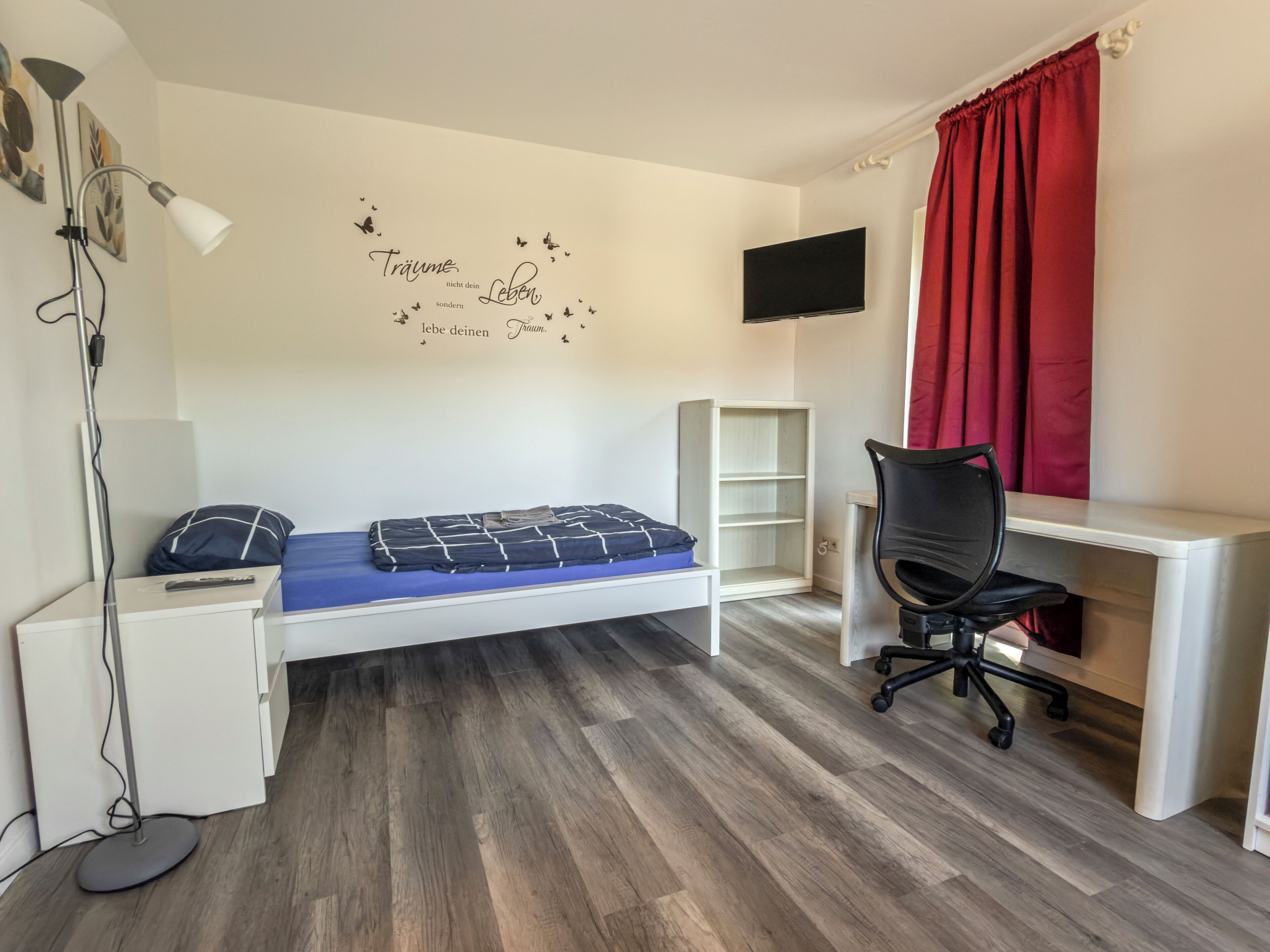 Un dormitorio con cama, escritorio, silla, televisor y un adorno en la pared.