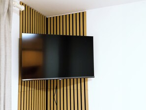 Seinälle asennettu litteänäyttöinen televisio, jonka takana on puisten listojen muodostama koristeellinen rakenne.