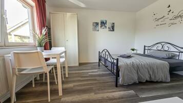 Een slaapkamer met een bed, een bureau met stoelen, een radiator en een raam met gordijnen.