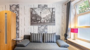 A bedroom with a bed, a wooden wardrobe, a small table, a picture on the wall, a window with curtains, and a radiator. - Apartment 'Old Town  in The Center At' with Wi-Fi (Flensburg)