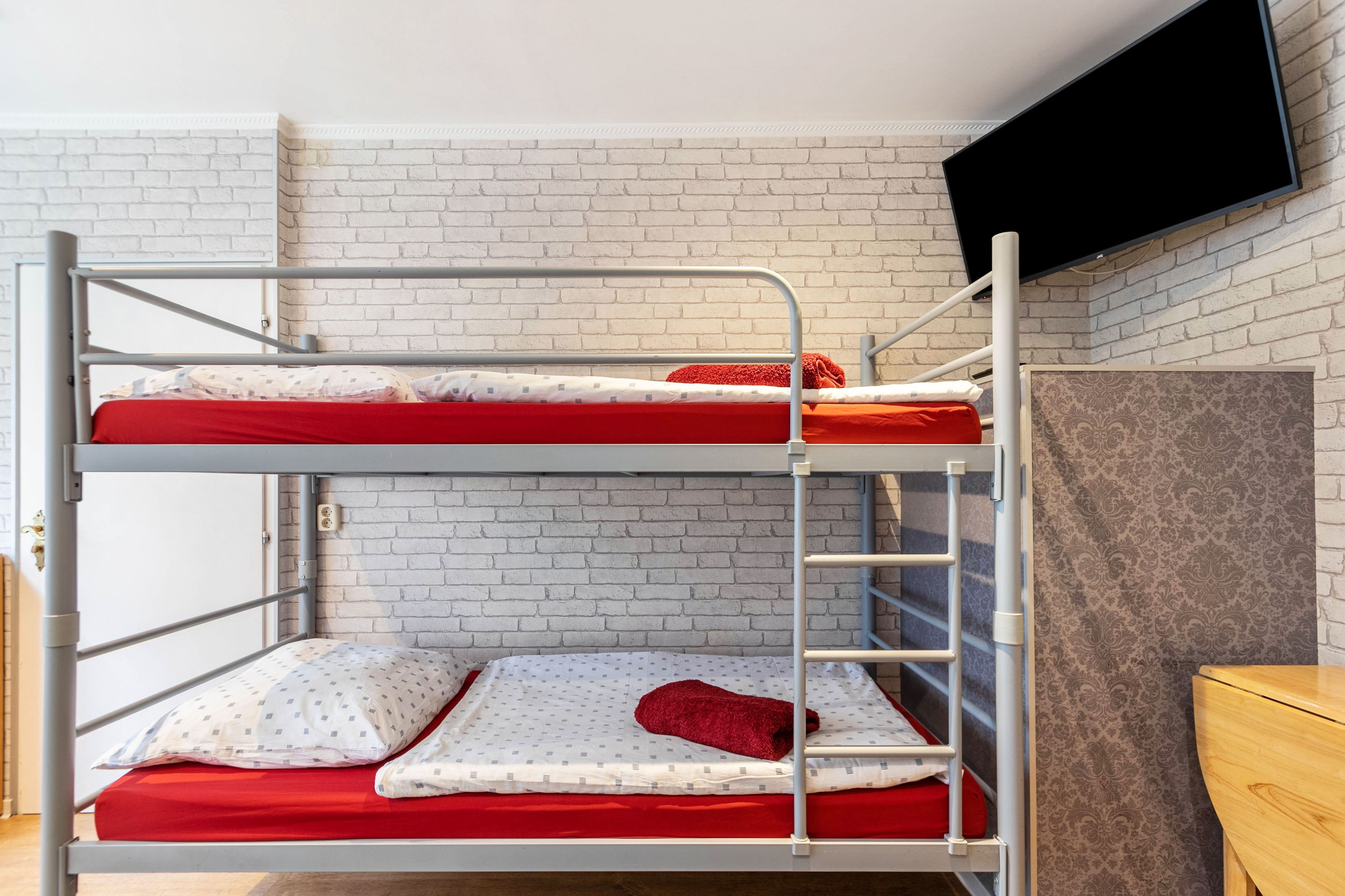 A bunk bed with two levels, a television mounted on the wall, and a patterned wallpaper on the adjacent wall.