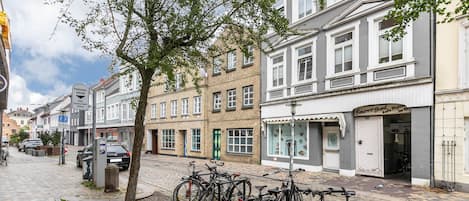 Een straat met geparkeerde fietsen, een boom en gebouwen met winkels.