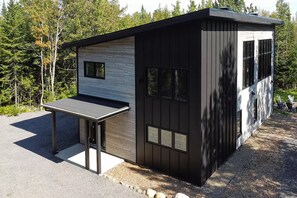 Eine moderne, zweigeschossige Hütte mit Flachdach, großen Fenstern und einer kleinen Außen-Sitzgelegenheit.