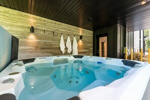 A hot tub with a wooden wall backdrop and a door leading outside. - Maison ULLR | Zen Retreat | 10 min to Le Massif (Petite-Rivière-Saint-François)